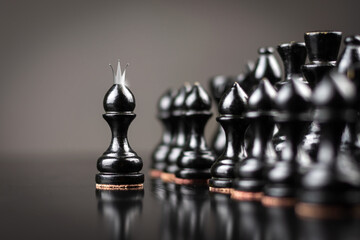 Black pawn with crown, in front of black pieces. Focus on the pawn. Reflection. Self Confidence. Achievement of the goal. Strategy. The game. Sport. Business.
