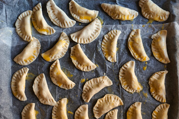 Greased ravioli on parchment paper. A tray of ravioli is about to be baked. Dinner with friends, homemade ravioli with meat and vegetables. Italian cuisine and culture.  