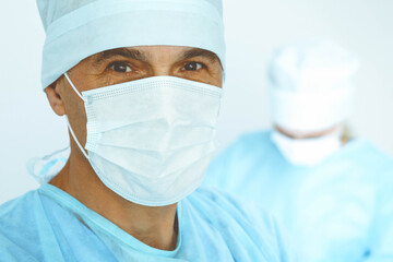 Fototapeta na wymiar A male surgeon headshot, a group of surgeons is operating in the background. Health care concept