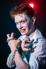 Maniac with joker makeup on his face and chain in his hands against the background of smoke illuminated by red light