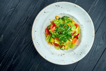 Diet and vegetarian salad of mixed vegetables and lettuce with peanut sauce, served in a white plate on a black wood background