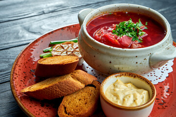 Traditional Ukrainian borscht with rib and sour cream, served in a red plate with rye bread and aromatic butter on a dark background. Red soup