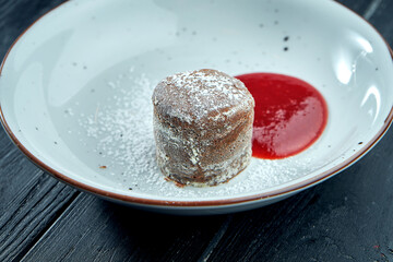 Dessert chocolate fondant with berry sauce and powdered sugar in a white plate on a dark background. Appetizing muffin