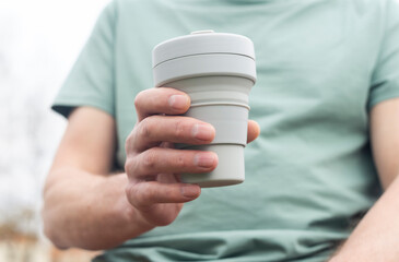 Collapsible cup for takeaway coffee or tea. Male hand with sustainable silicon mug. Eco lifestyle.