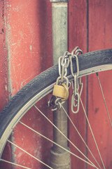 Bicycle chained to a pole. Lock and chain on bicycle wheel. Lock a bicycle with chain and pole on footpath. Toned image.