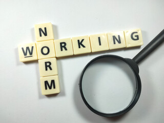 Selective focus.Scrabble letters with text NORM WORKING and magnifying glass on white background.