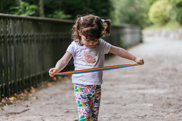 Little girl with pigtails, colourful trousers and white t-shirt, holding a rainbow ribbon in her hands while walking, symbol of LGBT. Concept of free education in the face of diversity.