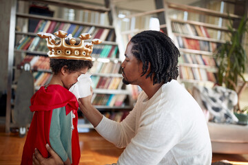 A cute little boy blow the nos with a help from his father while playing at home. Family, together, love, playtime