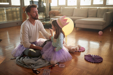 A young father waiting for his little daughter to put some lipstick on his lips while preparing for...