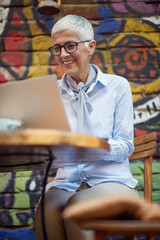 elderly caucasian female sitting at the table looking at her laptop, smiling
