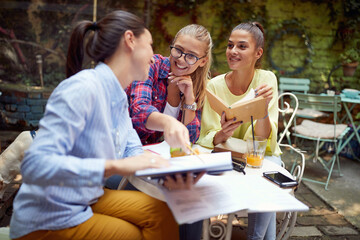 young adult caucasian females studying together in outdoor cafe, having fun
