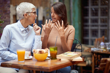 young adult woman talking to elderly female in outdoor cafe, having breakfast together