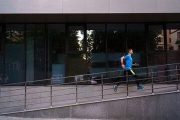 Man running in the city with a glass building in background. Fitness, workout, sport, lifestyle concept.