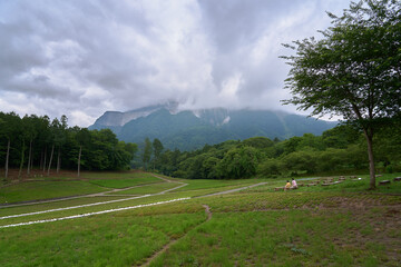 Two people relaxing in a field where you can see a mountain covered with clouds