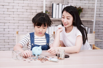 Smiling Asian little asian girl child is putting coins into piggy bank for saving money for the...