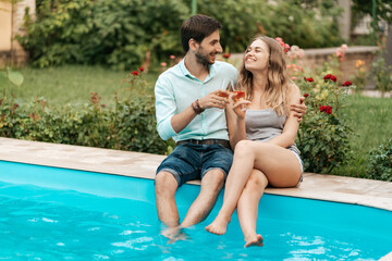 Fototapeta na wymiar Summer holidays, people, romance, dating concept, couple drinking sparkling wine while enjoying time together sitting at the pool