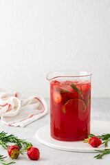 Fresh strawberry and lime drink with ice and rosemary in a jug close-up, summer refreshing lemonade