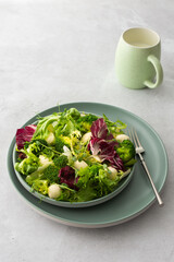 Top view of a table and a plate with light salad, green mix salad with broccoli, mozzarella cheese and microgreens and a mug of milk