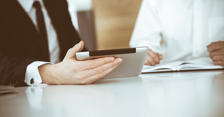 Unknown business people using tablet computer in modern office. Businessman or male entrepreneur is working with his colleague at the desk
