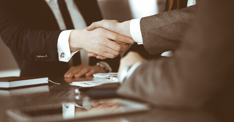 Obraz premium Unknown businessman shaking hands with his colleague or partner above the glass desk in modern office, close-up. Business people group at meeting
