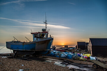 A fishing boat on the beach at sunset surrounded by equipment. Taken on Hythe Beach, Kent, UK