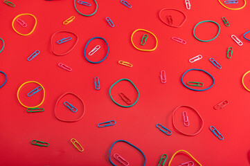 Stationery rubber bands and paper clips on a red background. Red background with a pattern.