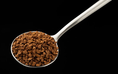Instant granulated coffee in spoon on black background