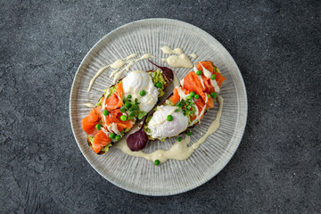 Whole wheat bruschetta with fresh salmon, guacamole, poached eggs and green peas. Ready menu for the restaurant. Neutral gray blue textured background.