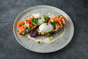 Whole wheat bruschetta with fresh salmon, guacamole, poached eggs and green peas. Ready menu for the restaurant. Neutral gray blue textured background.
