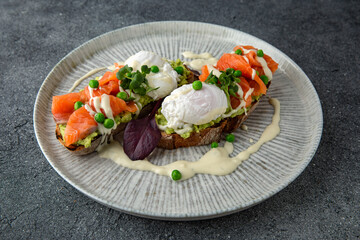 Whole wheat bruschetta with fresh salmon, guacamole, poached eggs and green peas. Ready menu for the restaurant. Neutral gray blue textured background.