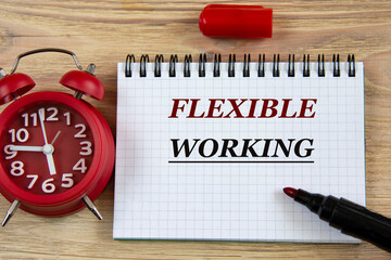 FLEXIBLE WORKING - words in a notebook on a wooden background with an alarm clock and a marker