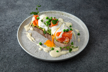 Whole wheat bruschetta with fresh salmon, guacamole, poached eggs and green peas. Ready menu for the restaurant. Neutral gray blue textured background.