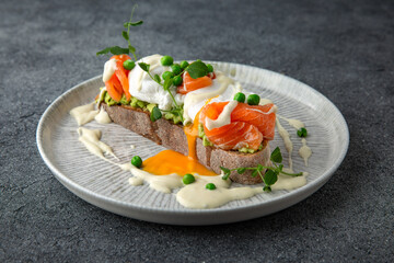 Whole wheat bruschetta with fresh salmon, guacamole, poached eggs and green peas. Ready menu for the restaurant. Neutral gray blue textured background.
