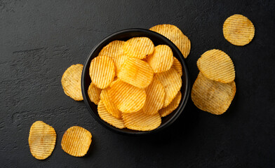 Ridged potato chips in bowl on black background, top view