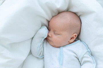 newborn baby boy sleeps seven days in a cot at home on a cotton bed, close-up