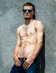 A young and sexy man is leaning against a marble wall with aviators wearing glasses.