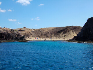 Fototapeta premium View of a bay with big sandy beach and many bathers between some rocks with deep blue sea on Lanzarote