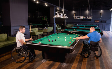 Adult men with disabilities in a wheelchair play billiards in the club