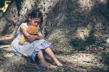 Sad girl hugging teddy bear sitting under tree sadness alone in green park. Lonely girl feeling sad unhappy sit outdoors hug best friend toy. Autism child play teddy bear best friend. Family violence