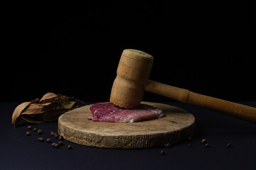 A kitchen hammer and a piece of meat next to it. Wooden kitchen hammer for meat. Meat on black...