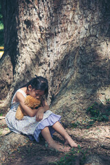 Sad girl hugging teddy bear sitting under tree sadness alone in green park. Lonely girl feeling sad unhappy sit outdoors hug best friend toy. Autism child play teddy bear best friend. Family violence
