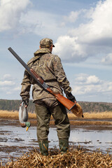 hunter with a duck decoys in both hands stands in front of the swamp