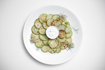 top view of fried zucchini slices with sour cream on plate on white background
