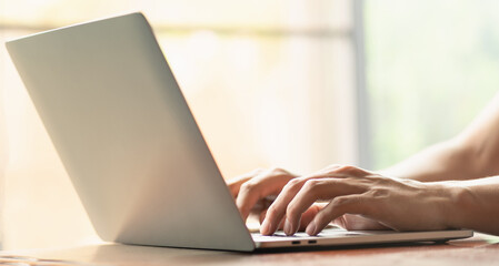 man is using a laptop to search for business information, stocks on desk and communicate using social media with colleagues using the Internet. Closeup hands typing keyboard and free copy space