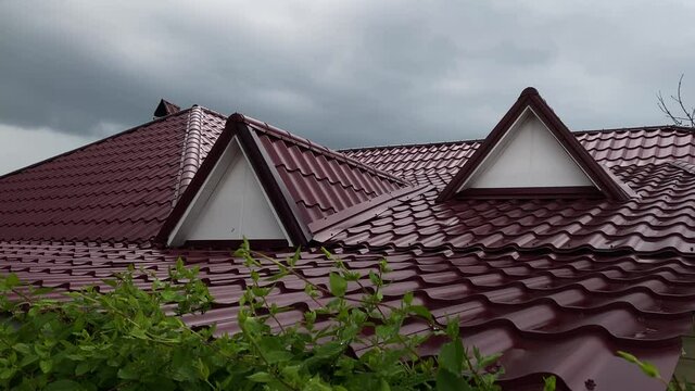 View of red metal roof of house in rainy day on background of cloudy sky.