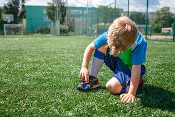 Young soccer player looks at the boots torn during the game on the football field, hard training,...
