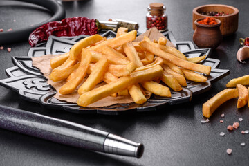 Tasty fried french fries with salt and spices on a dark background