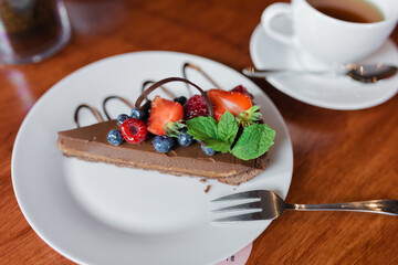 Piece of cake with chocolate and berries on plate on wooden table in cafe