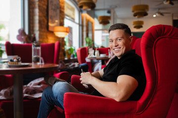 Young confident business man sitting on red armchair at a table in cozy cafe