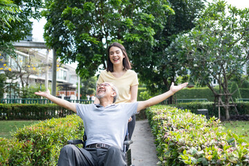Asian daughter pushing father sitting on wheelchair in the public park	